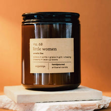 Load image into Gallery viewer, Candle jar labeled 'little women' on a stone surface with an orange background
