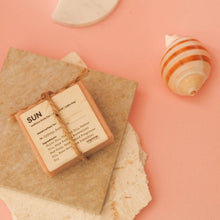 Load image into Gallery viewer, Soap bar with text 'SUN' on a textured surface with a shell and moon-shaped object.
