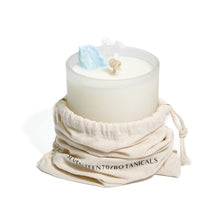 Load image into Gallery viewer, White candle in a glass holder with decorative elements, wrapped in a branded cloth bag on a white background.
