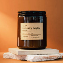 Load image into Gallery viewer, Candle jar labeled 'wuthering heights' on a stone surface with an orange background

